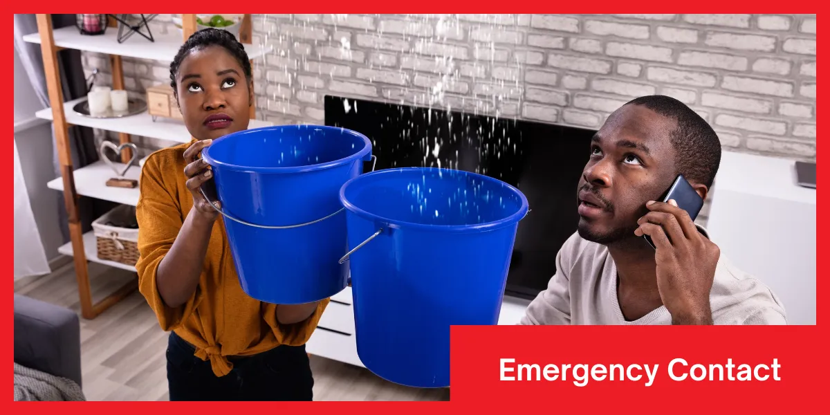 Two people in a flooded room holding buckets to catch water while the other is calling for emergency help.