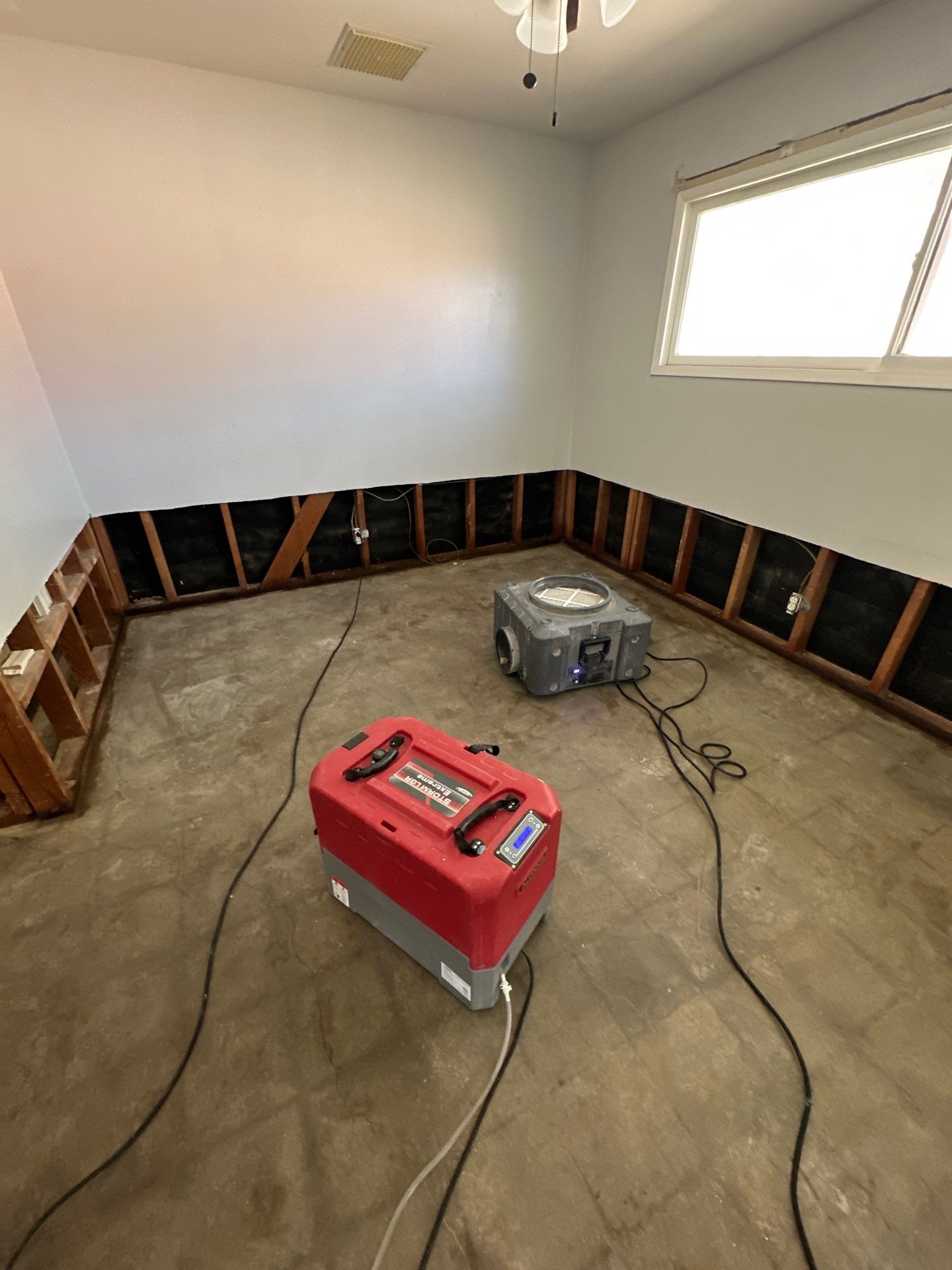 Air movers and dehumidifier drying a water-damaged room with exposed studs in Lancaster, CA